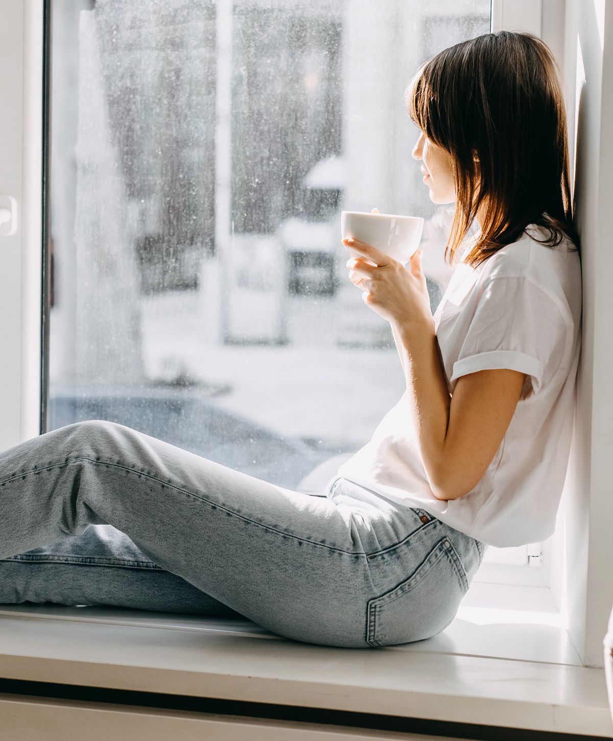 Woman enjoying tea by a sunlit window.