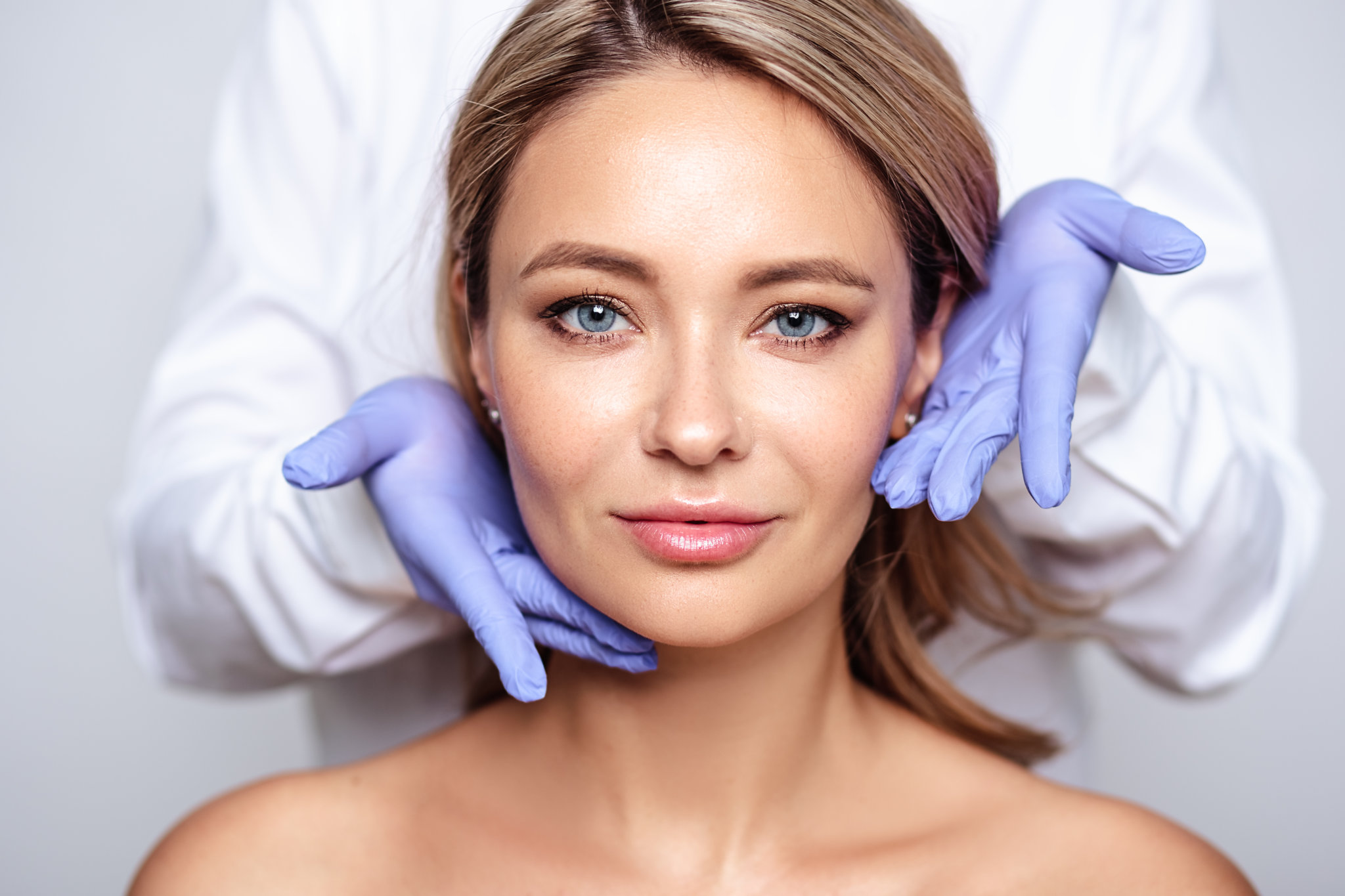 Close up portrait of young blonde woman with cosmetologyst hands